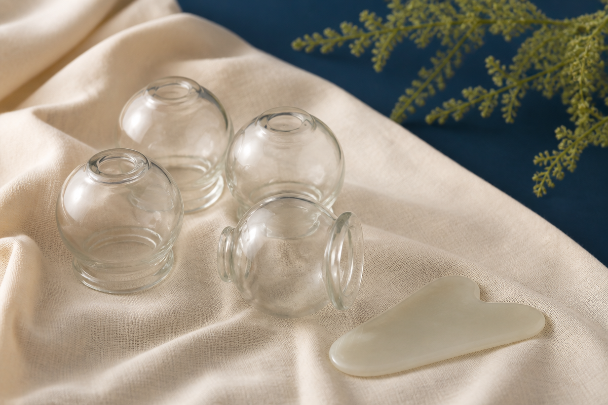 Clear glass cupping jars and a smooth guasha tool on ivory linen
